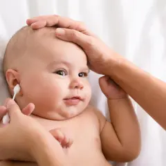 Delikatne czyszczenie uszu niemowlaka. Mama ostrożnie używa patyczka higienicznego, by zadbać o higienę maluszka.