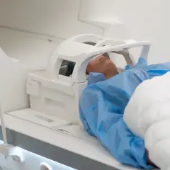 Pacjent leży w aparacie do rezonansu magnetycznego. Czy rezonans głowy obejmuje uszy? Tak, specjalna cewka jest umieszczona wokół głowy, zakrywając uszy.
