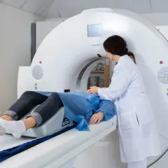 Pacjent na stole do tomografii komputerowej, pielęgniarka przygotowuje badanie. Czas oczekiwania na wynik TK na SORze bywa długi.