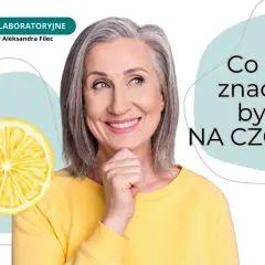 Uśmiechnięta kobieta zastanawia się, co to znaczy być na czczo. Obok cytryna i napis "BADANIA LABORATORYJNE".
