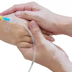 Ciepłe dłonie obejmują rękę z wenflonem, symbolizując wsparcie i troskę w trudnych chwilach.