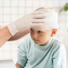Chłopiec z opatrunkiem na głowie po uderzeniu w czoło. Lekarz zakłada mu bandaż.