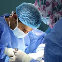 Chirurg skupiony na pracy, używa narzędzi do zabiegu z użyciem szwów rozpuszczalnych w jamie ustnej.
