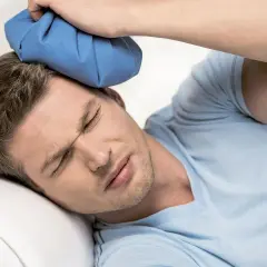 Mężczyzna z zamkniętymi oczami przykłada zimny okład do głowy po mocnym uderzeniu.