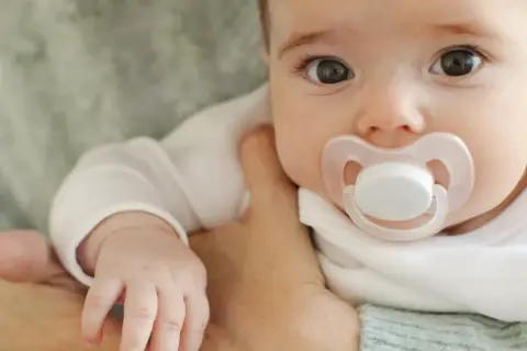 Malutkie dziecko z wielkimi oczami i smoczkiem w buzi. Czas pomyśleć, jak odzwyczaić dziecko od smoczka, by mogło swobodnie odkrywać świat.