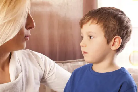 Kobieta rozmawia z chłopcem, który ma problemy z mową. Wsparcie w walce z afazją u dzieci.