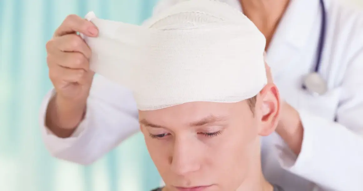 Lekarz opatruje głowę młodego mężczyzny, który doznał urazu aksonalnego mózgu.